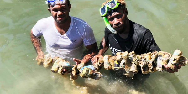Two divers with some of the old cans collected during the clean-up. Photo, Dive Gizo.
