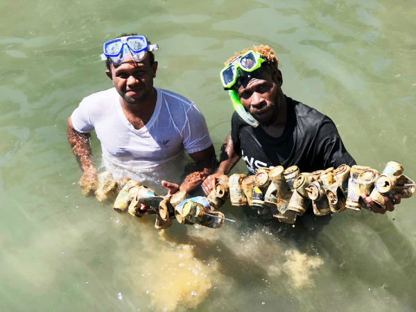 Two divers with some of the old cans collected during the clean-up. Photo, Dive Gizo.