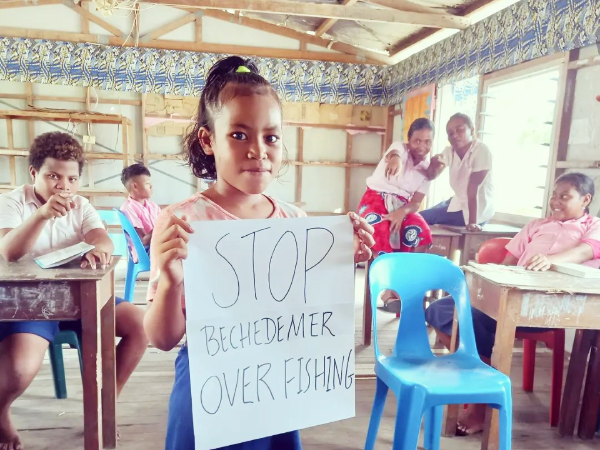 A young female student displaying a poster with a message ‘Stop Beche-de-mer over fishing’ in peaceful protest.