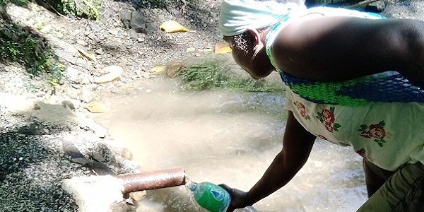 A villager refilling a bottle from a pipe at a stream.