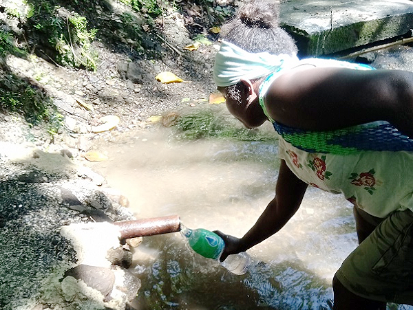 A villager refilling a bottle from a pipe at a stream.