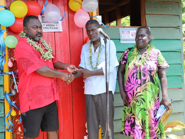 Hon Tausina hands over keys to solar grid power house to school principal whilst Mrs Turanga looks on.