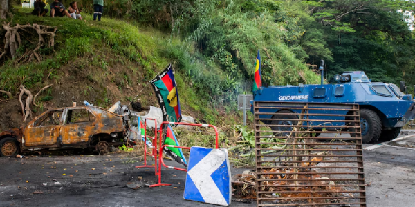 The Kanak flag flies at a road block set by protesters as French officers arrive to dismantle it. (AFP: Delphine Mayeur)