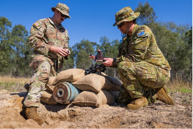 Personnel from the United States Army and the Australian Army apply a rocket wrench to an inert bomb during mission-specific training for Operation Render Safe, RAAF Base Amberley, Queensland
