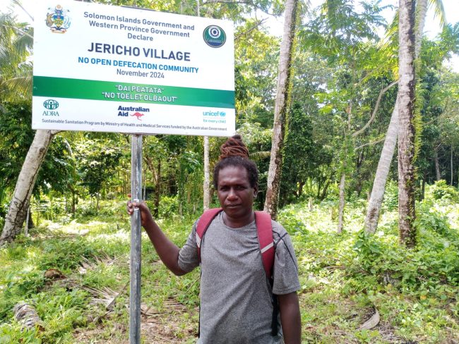 Chris Panakera taking photo Infront of signboard at his community in Rannogah.