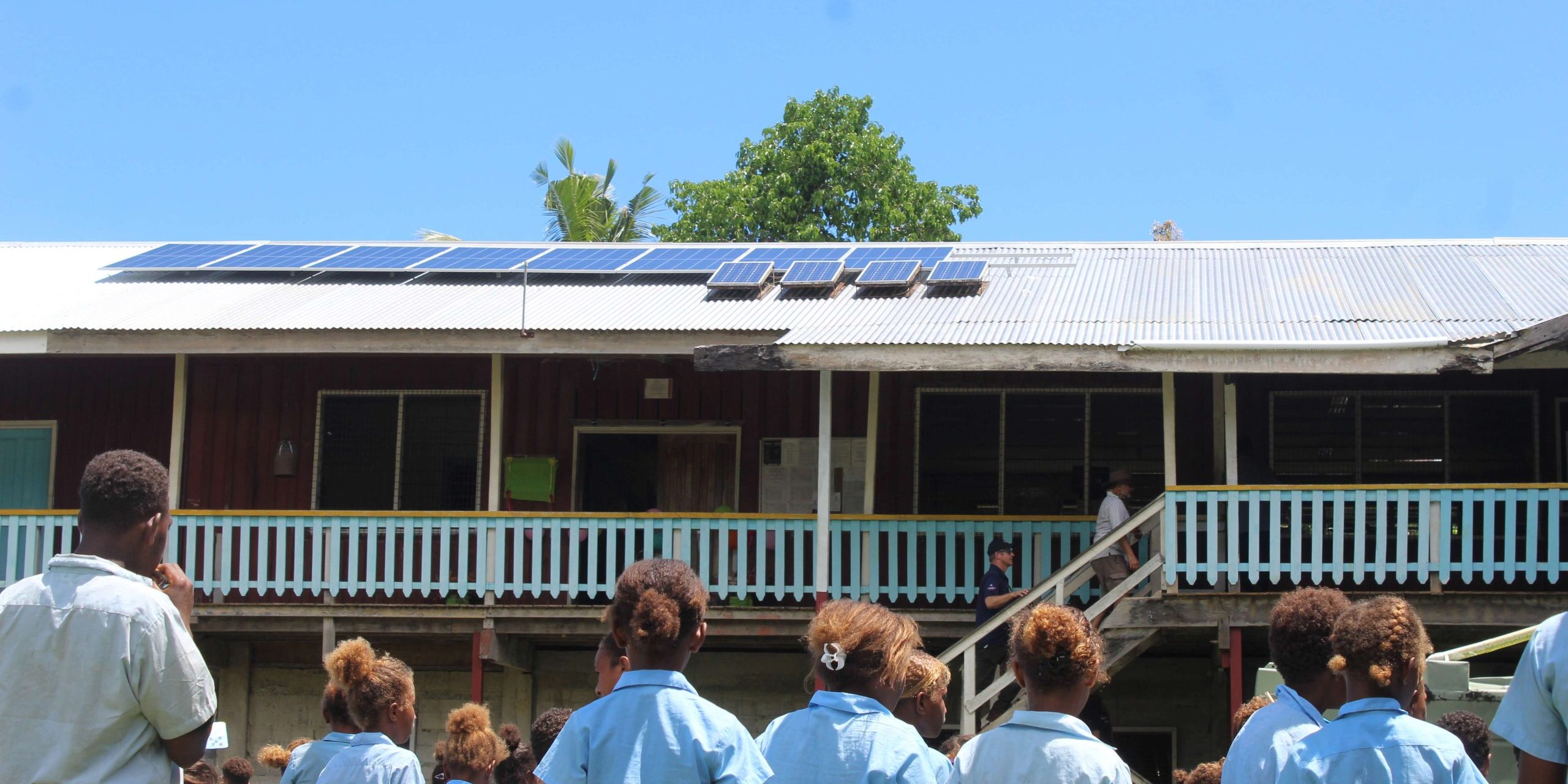 Solar panels installed on top of a Talakali classroom at student looks on